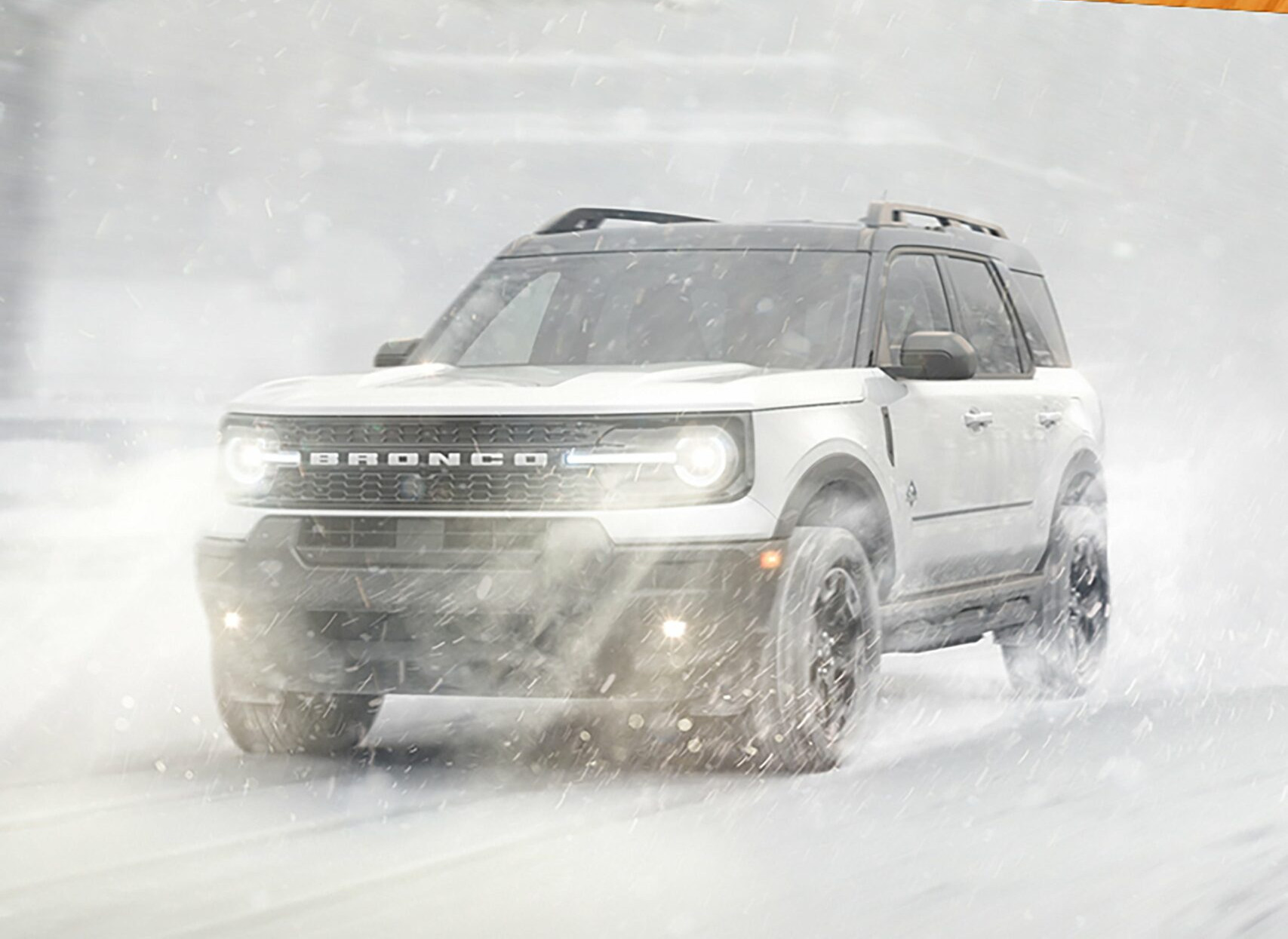 A white 2026 Ford Bronco Sport driving through heavy falling snow with its lights on