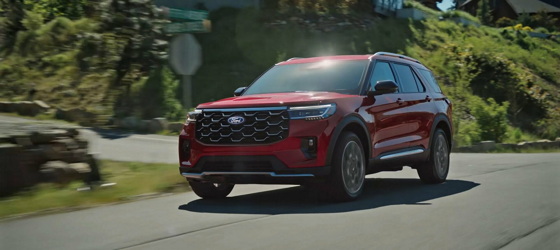 A red 2027 Ford Explorer on a two-lane road through forested hills