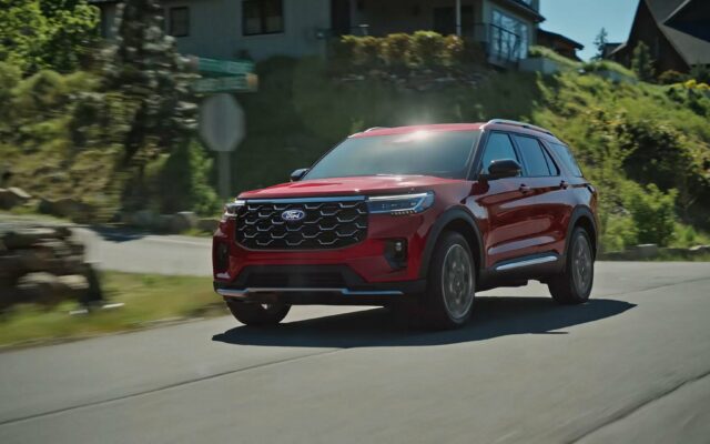 A red 2027 Ford Explorer on a two-lane road through forested hills