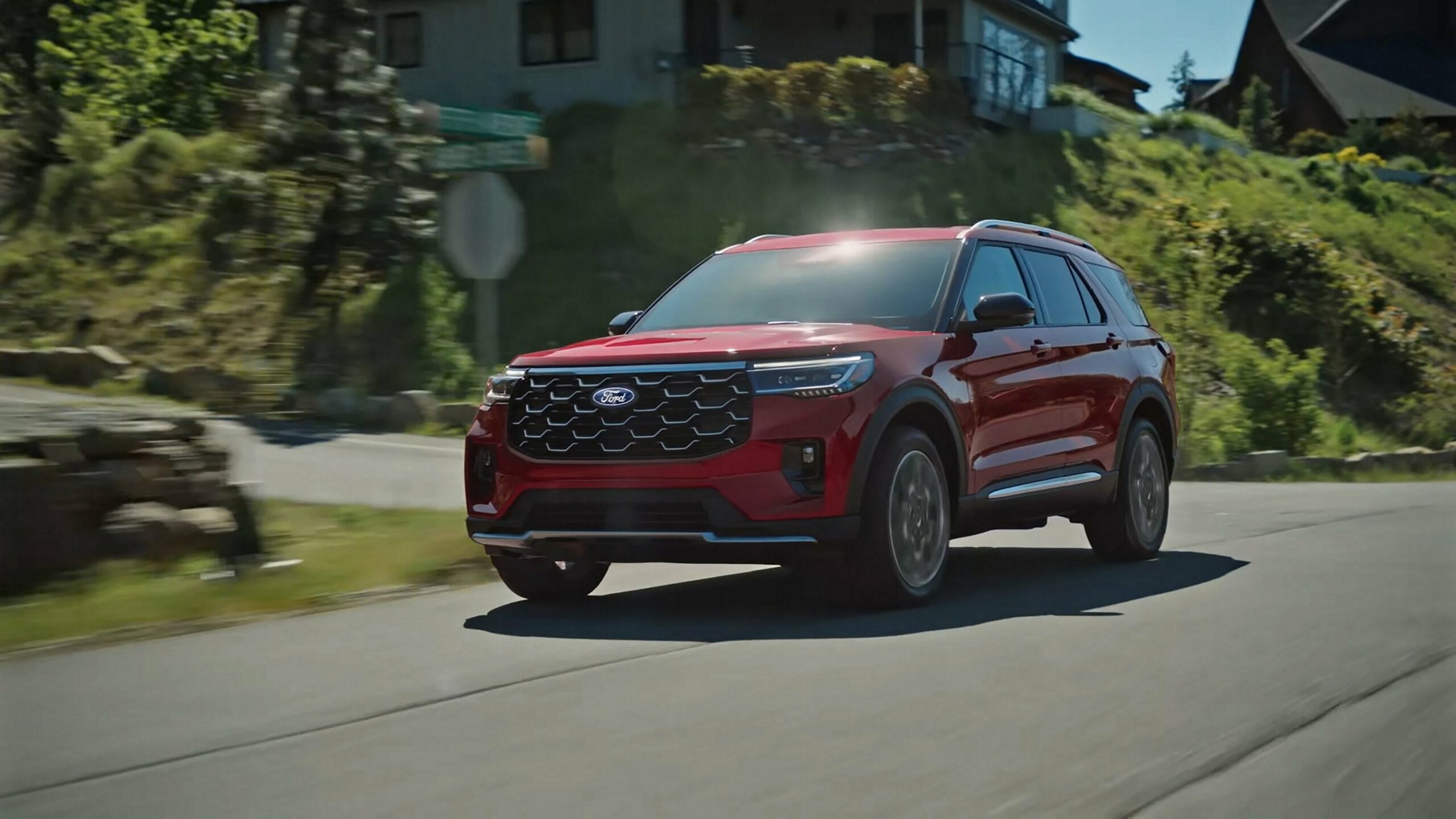 A red 2027 Ford Explorer on a two-lane road through forested hills.