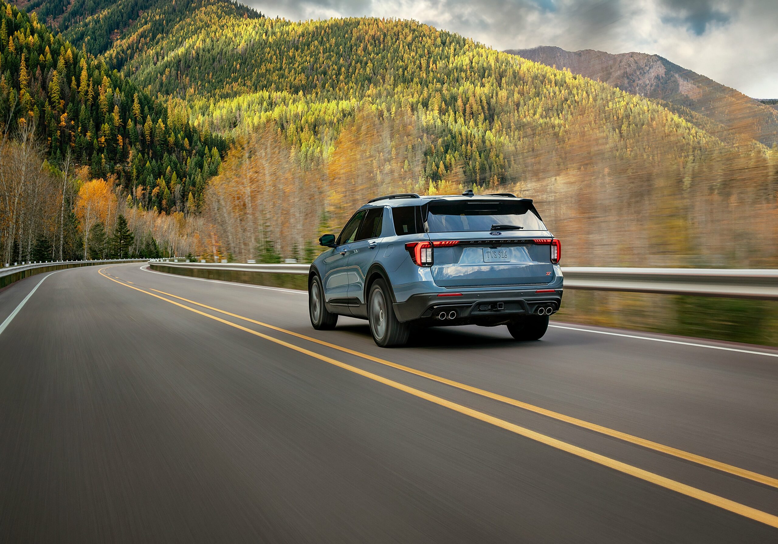 The rear of a light blue 2027 Ford Explorer on a mountain road in fall