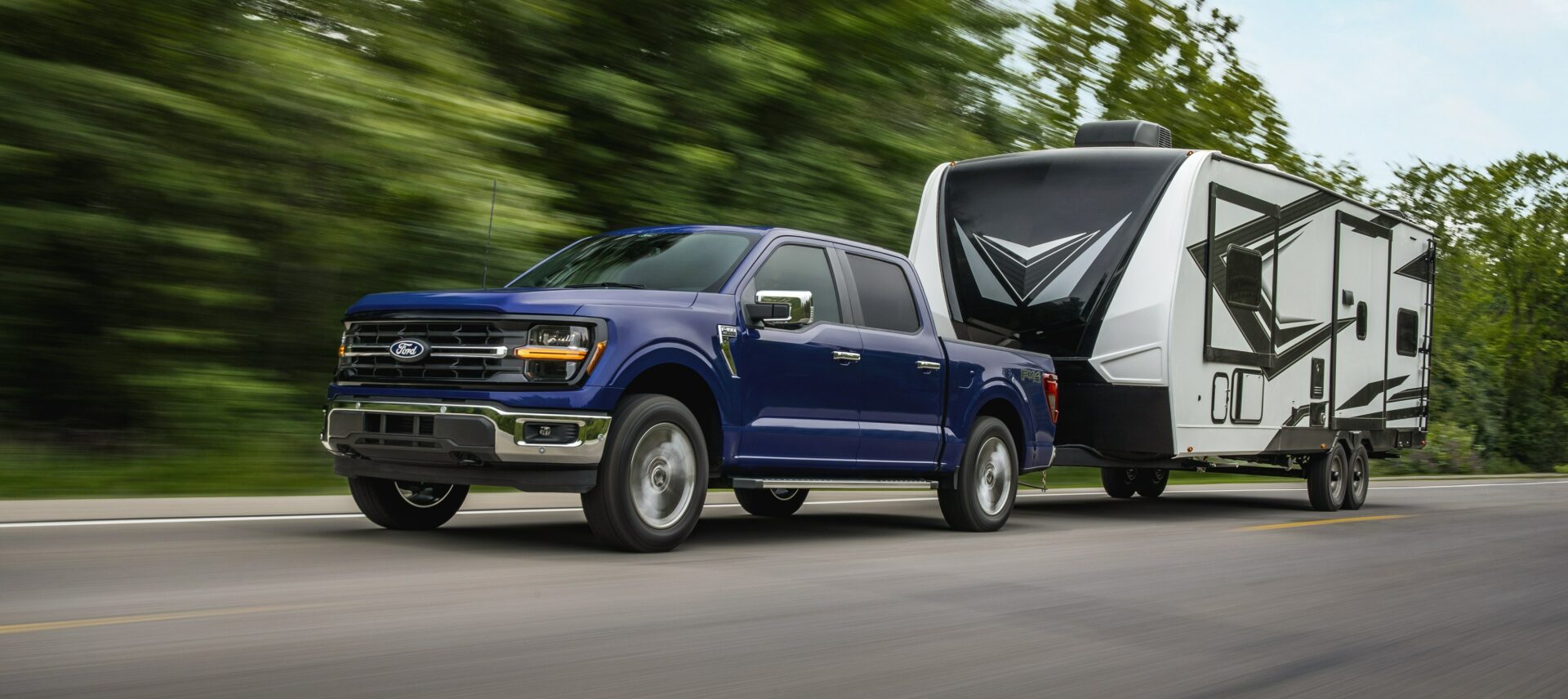 A dark blue 2026 Ford F-150 SuperCrew towing a white travel trailer along a highway