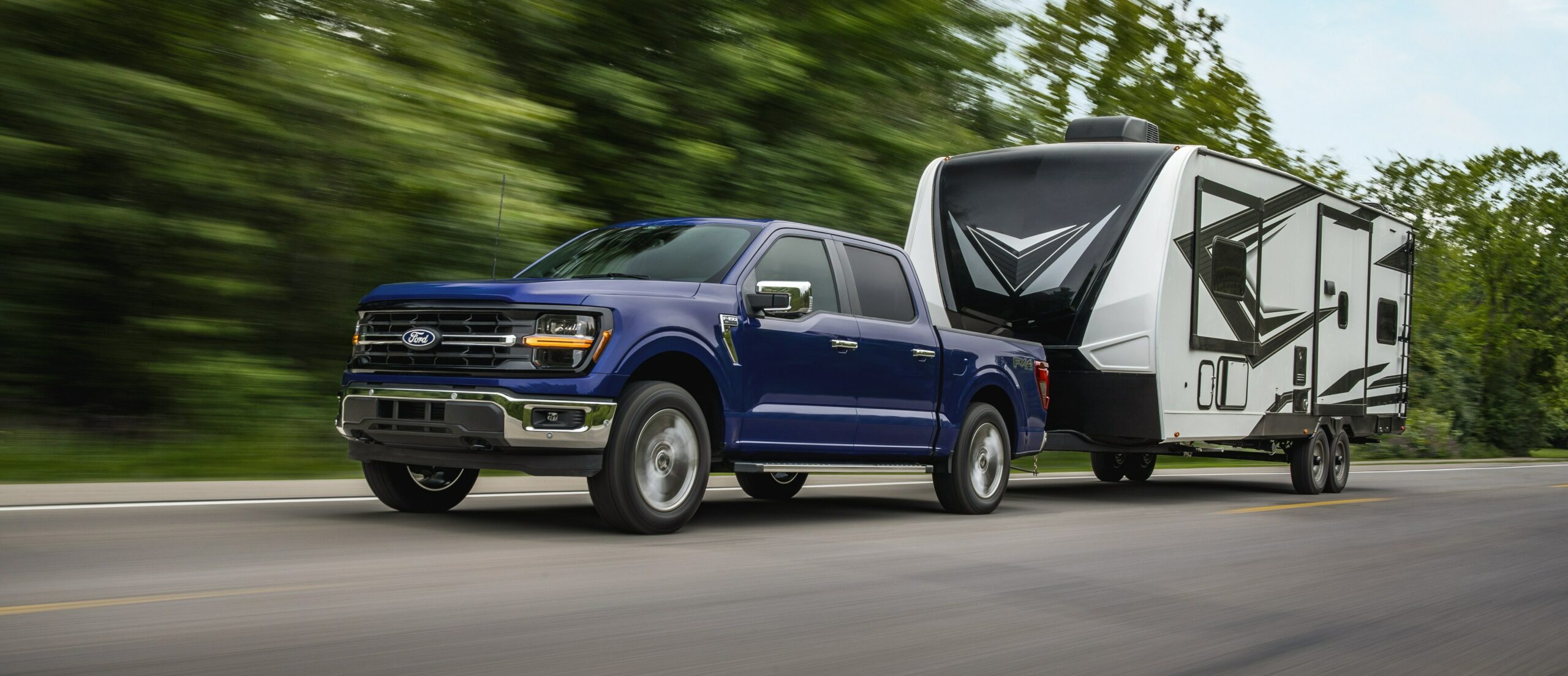 A dark blue 2026 Ford F-150 SuperCrew towing a white travel trailer along a highway
