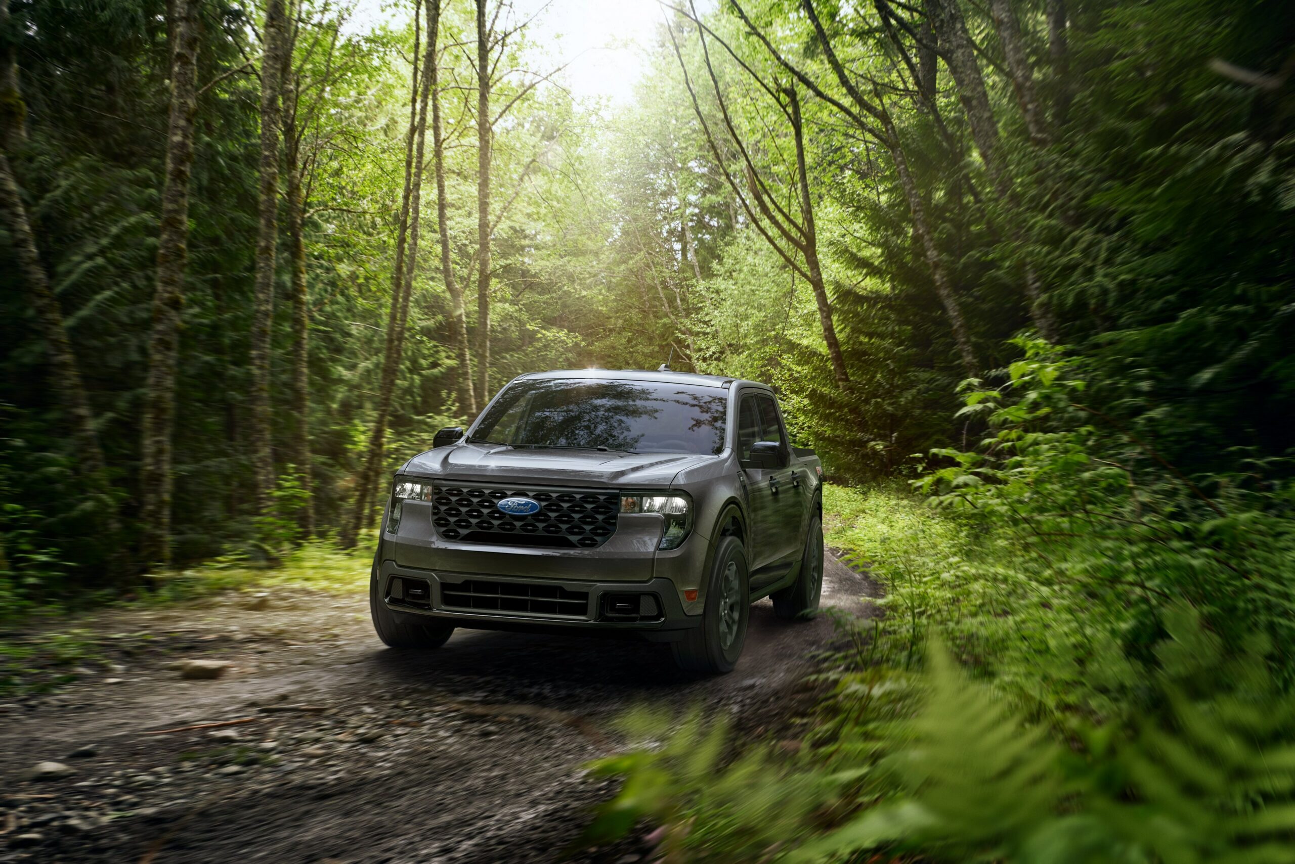 A dark green 2026 Ford Maverick driving a muddy trail through dense green forest