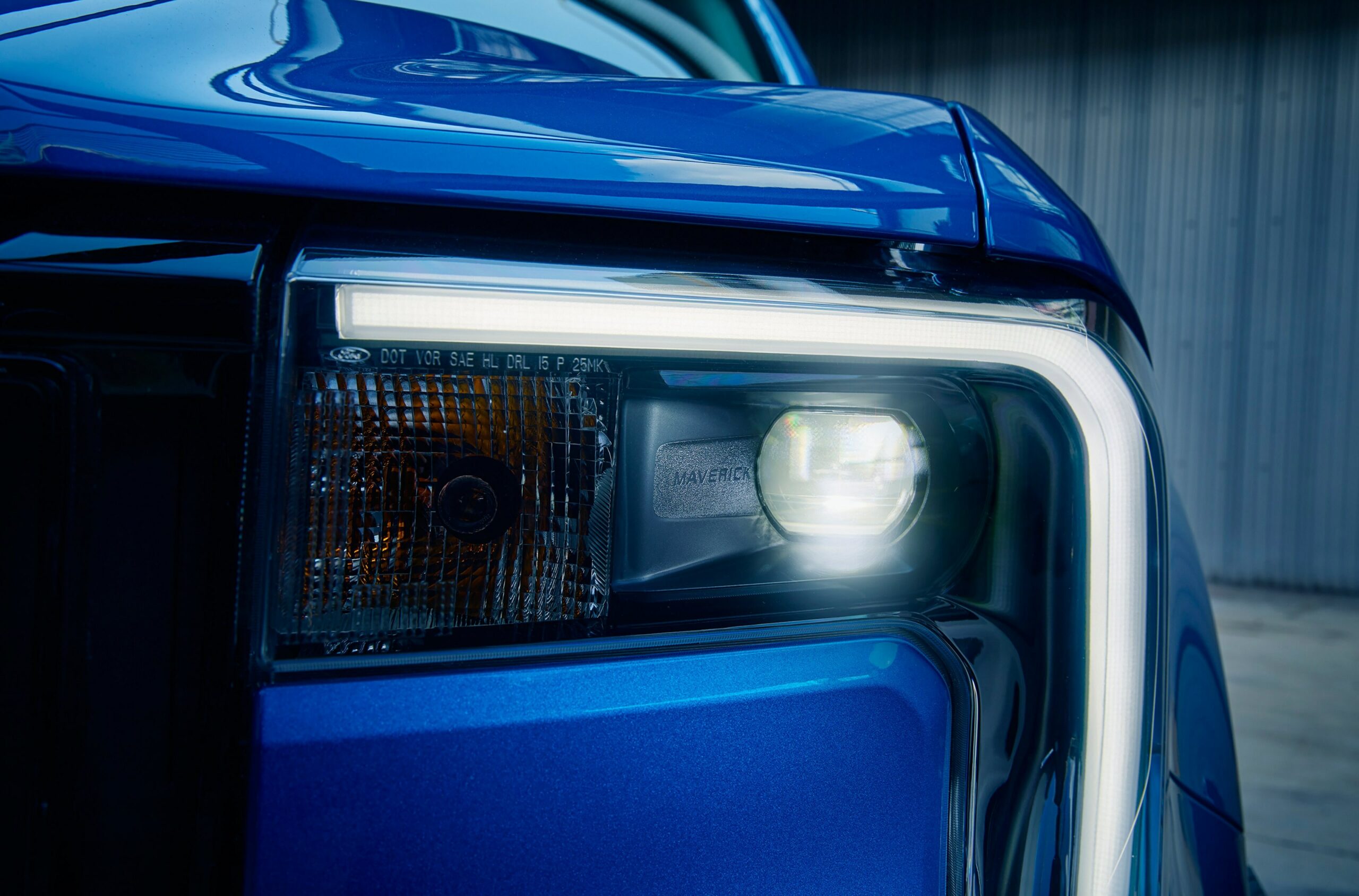 A close-up of the lit headlamp and daytime running light on a blue 2026 Ford Maverick