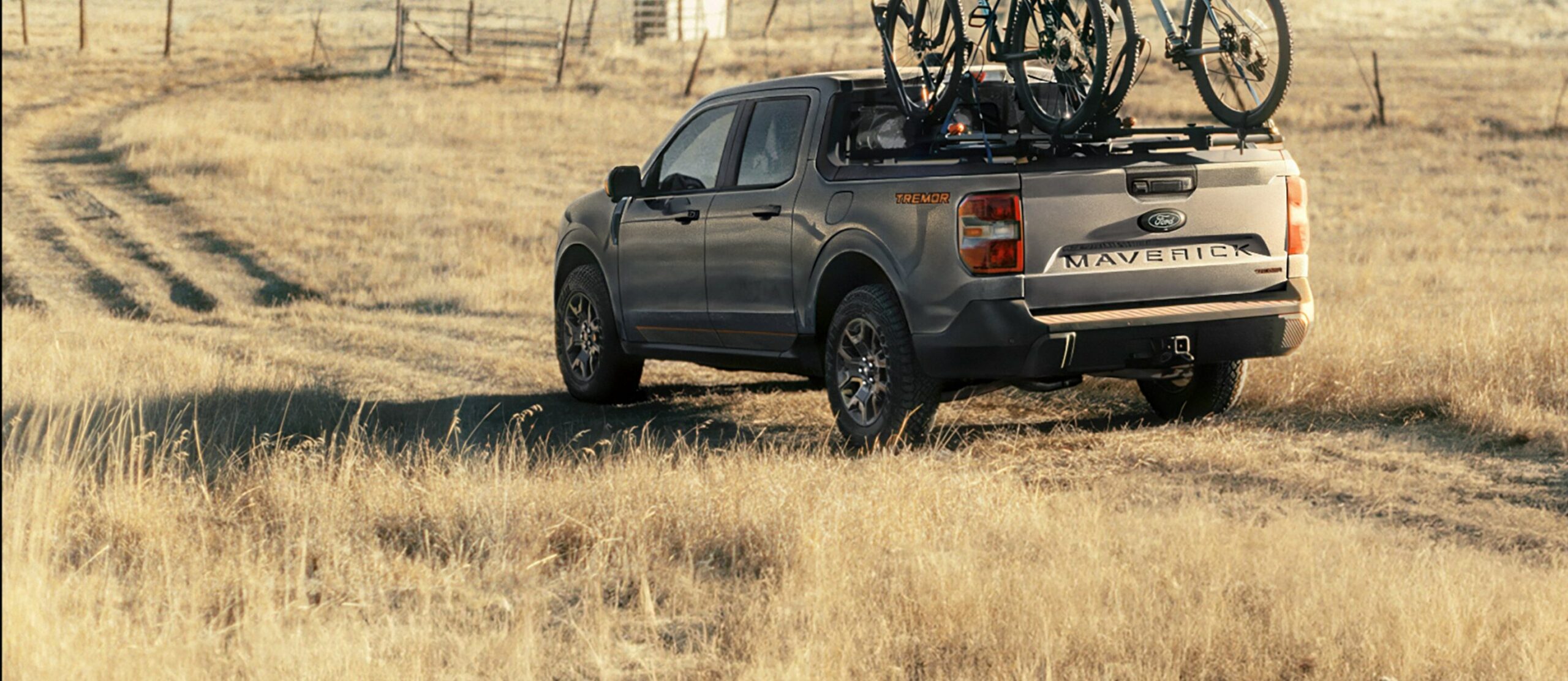 A gray 2026 Ford Maverick Tremor parked in a dry grass field with two mountain bikes on a bed rack