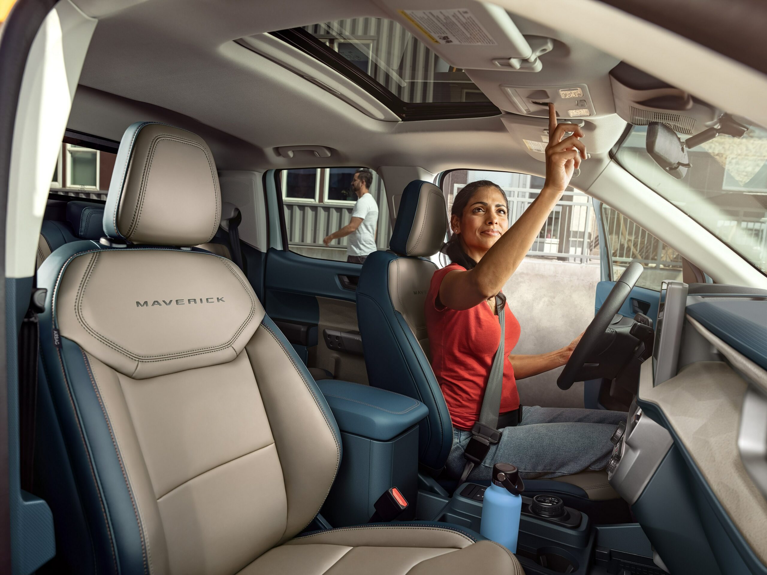 The cabin of a 2026 Ford Maverick with cream seats, a driver reaching up to the open moonroof