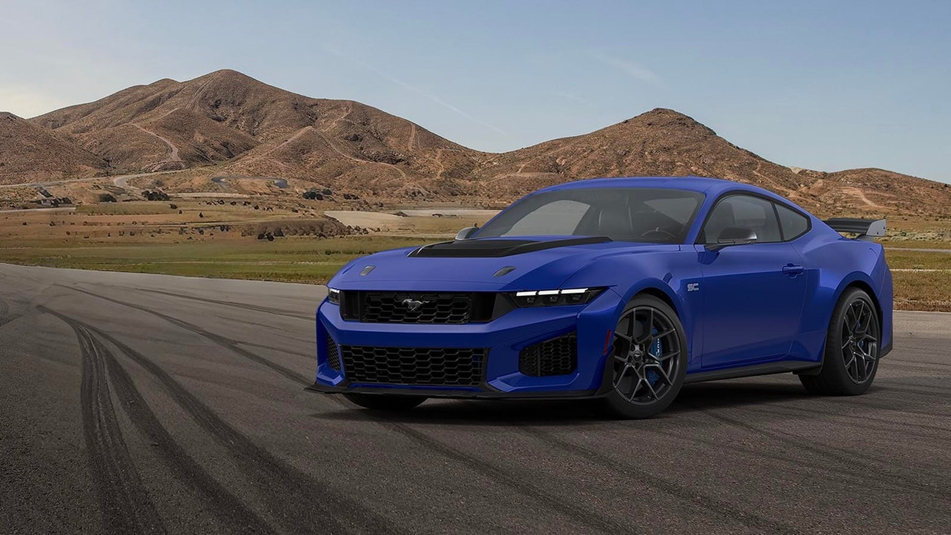 A blue 2026 Ford Mustang Dark Horse SC parked on a racetrack, with a rear wing, black hood vent and dark wheels