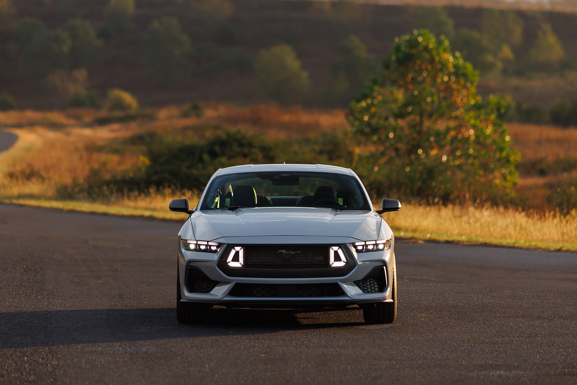 A gray 2026 Ford Mustang with the RTR Package facing the camera on an empty road at golden hour