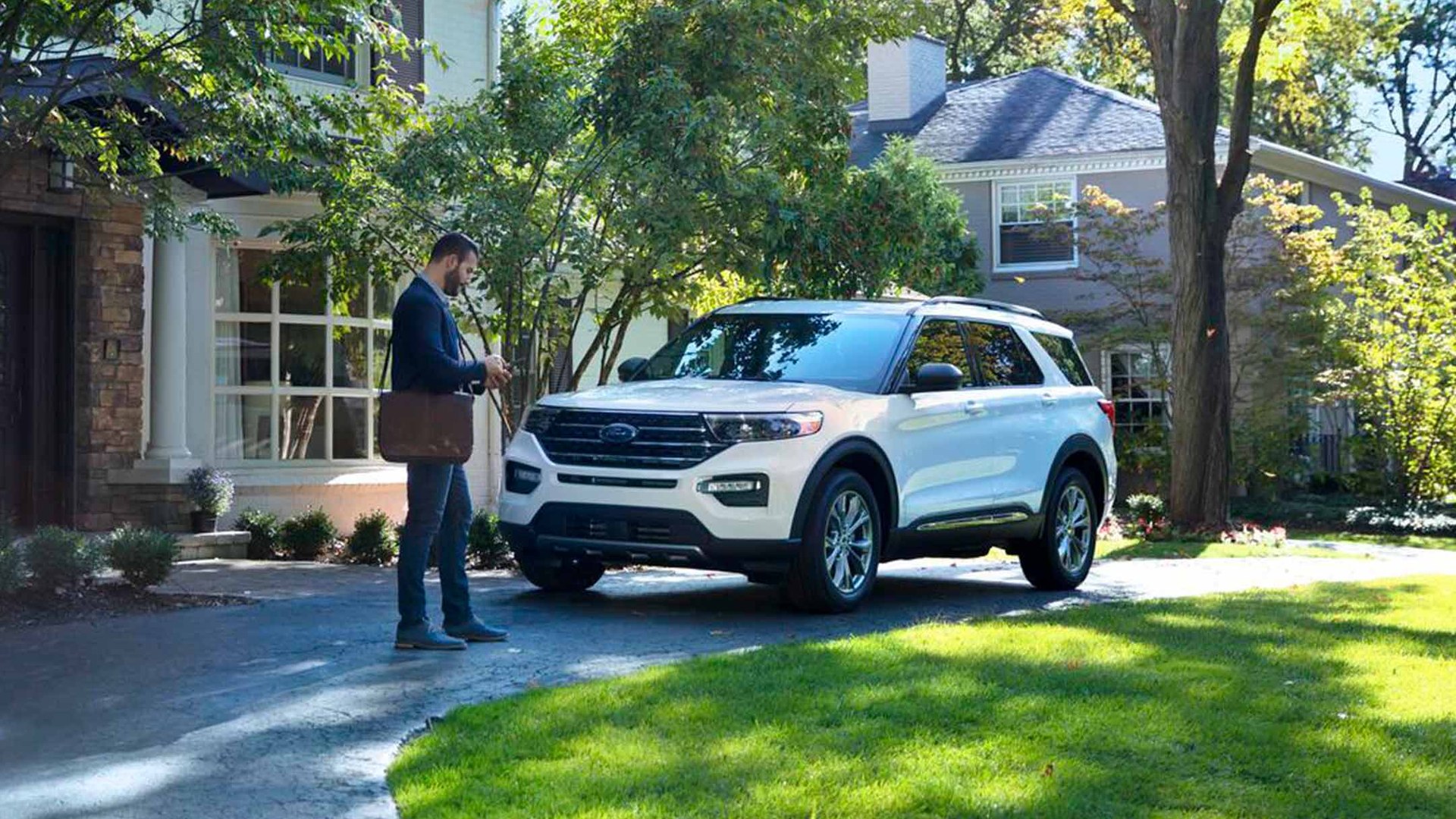 A white Ford Explorer on the driveway of a suburban house while its owner checks a phone