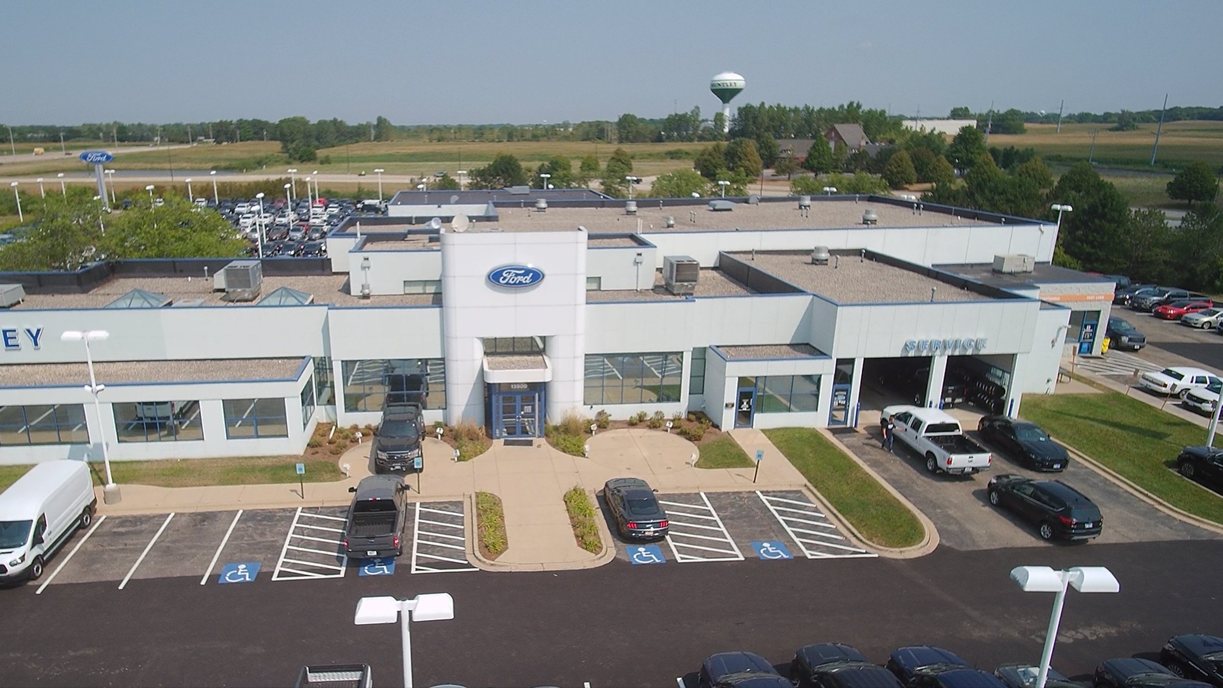 Aerial view of the Huntley Ford building on Automall Drive, with the showroom entrance under the Ford tower, the service drive to its right, and customer parking in front